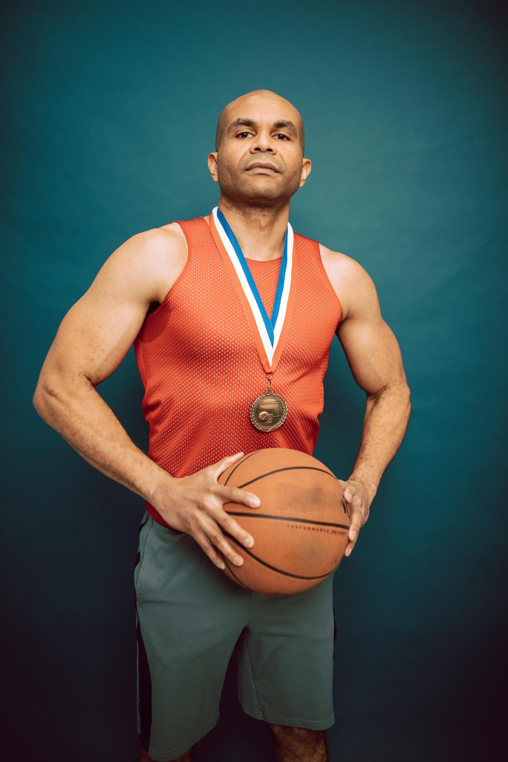 Confident basketball player holding ball and wearing medal, standing in sporty pose.